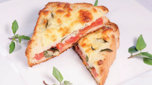 Croque-monsieur cortado ao meio com queijo gratinado, presunto e tomate