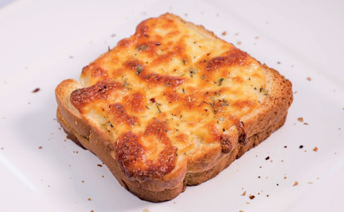 Croque-monsieur tradicional com cobertura de queijo gratinado dourado e ervas, sobre prato branco