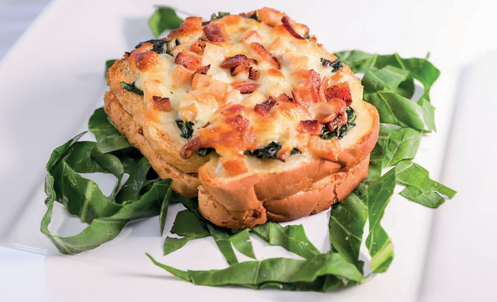 Croque-monsieur gratinado com queijo derretido, bacon e folhas verdes descansando sobre prato branco